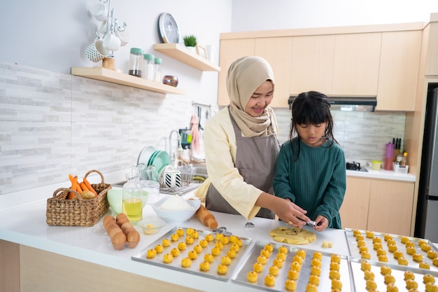 Madre musulmana asiática durante la actividad de ramadán con su hija haciendo un pastel nastar juntos en casa en la cocina para celebrar eid mubarak kareem