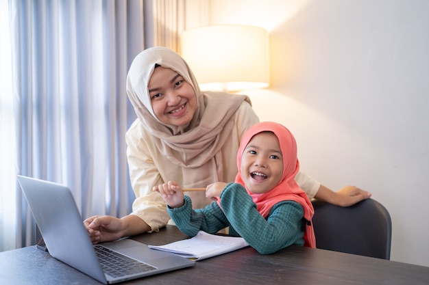 Madre musulmana asiática ayuda a su hija a aprender en línea usando la computadora portátil estudiando desde casa