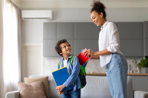 Madre negra prepara a su hijo con mochila y cuadernos para la escuela