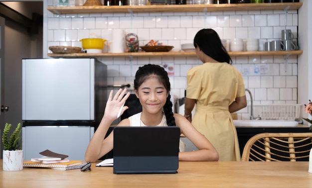 Madre y niña asiática aprendiendo y mirando la computadora portátil haciendo la tarea estudiando con el sistema de aprendizaje electrónico de educación en líneavideoconferencia de niños con profesor tutor en casa