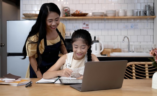 Madre y niña asiática aprendiendo y mirando la computadora portátil haciendo la tarea estudiando con el sistema de aprendizaje electrónico de educación en líneavideoconferencia de niños con profesor tutor en casa