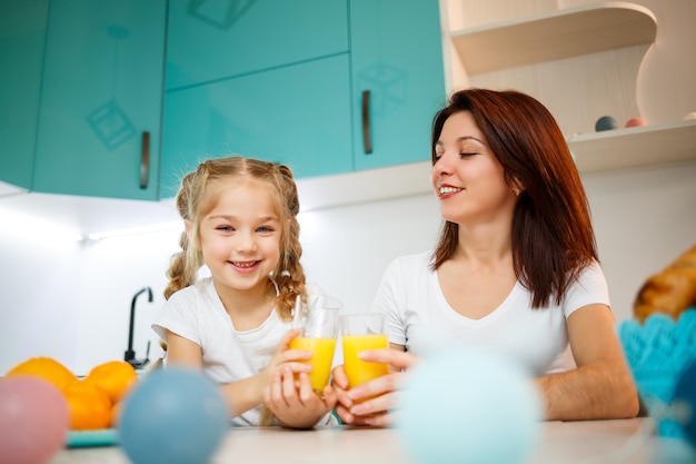 Madre con niña bebiendo jugo de naranja mientras desayunan juntos