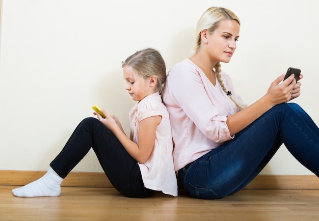 madre y niña jugando con teléfonos móviles de interior