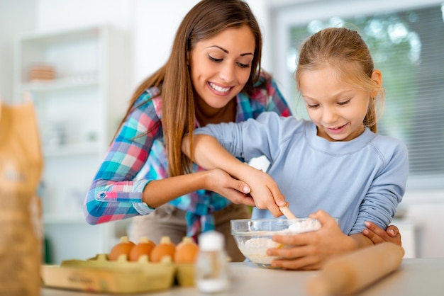 Madre y niña mezclando masa en la cocina doméstica. La madre le enseña a su hija cómo hacer las galletas.