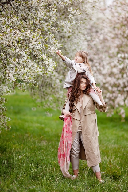 Madre con niña niño jugando en jardín floreciente de primavera. Mujer con hija abrazando y divirtiéndose al aire libre. Concepto de familia feliz