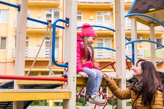 Madre con niña en el patio de recreo Mujer ayuda a su hija