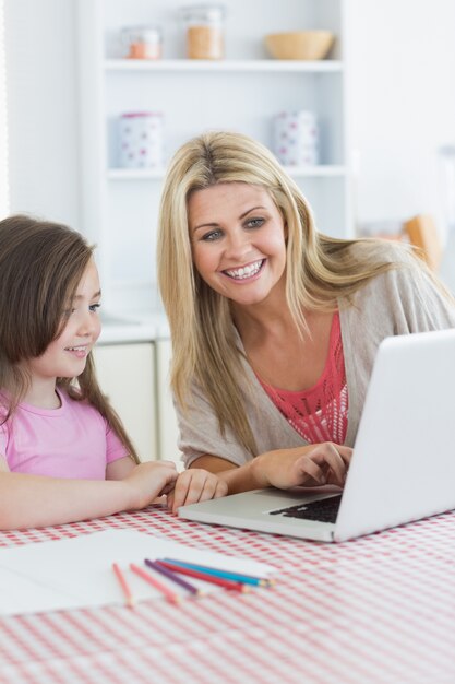 Madre y niña sentada en la cocina con la computadora portátil