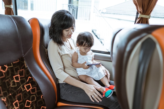 Una madre y una niña sosteniendo un teléfono celular mientras están sentadas junto a la ventana del autobús.