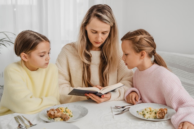 Madre y niñas rezando en la mesa de la cena