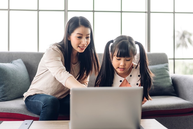 Madre y niño asiático niña aprendiendo y mirando la computadora portátil haciendo la tarea estudiando conocimientos con el sistema de educación en línea e-learning.Videoconferencia para niños con profesor tutor en casa