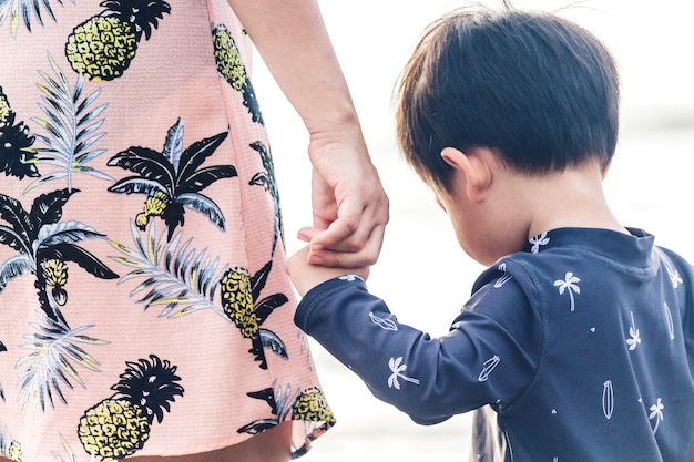 Madre y niño pequeño cogidos de la mano de pie en la playa. Amor del concepto de familia