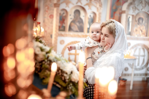 Foto una madre con un niño pequeño en una iglesia cristiana ortodoxa o templo reza o vino al sacramento del bautismo creyentes en un lugar santo en el altar o iconos