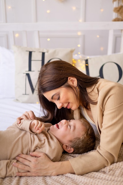 Una madre con un niño pequeño juega a abrazar y besar en casa en una cama en tonos marrones naturales una familia feliz con un niño pequeño se divierten juntos