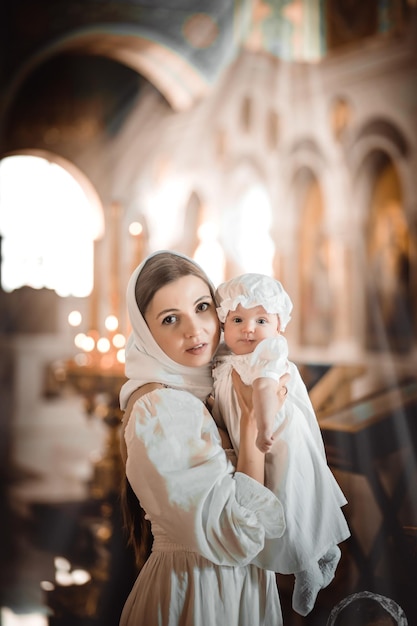 Una madre con un niño pequeño en un templo o iglesia reza cerca de un ícono y velas o vino a un servicio divino en la iglesia ortodoxa rusa el bautismo de un bebé