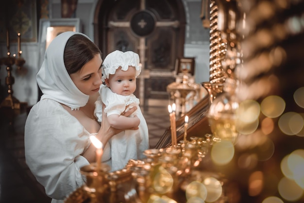 Una madre con un niño pequeño en un templo o iglesia reza cerca de un ícono y velas o vino a un servicio divino en la iglesia ortodoxa rusa el bautismo de un bebé