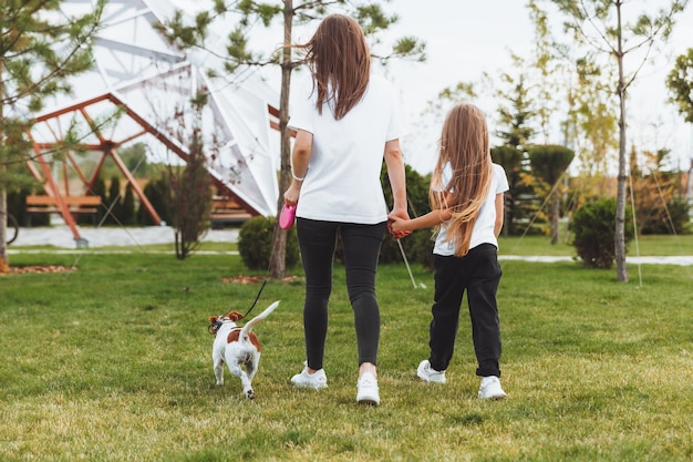 Una madre con un niño y un perro Jack Russell terrier están caminando juntos en el parque una mujer y una niña están paseando a su perro