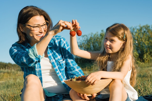 Madre y niño sentados en la hierba comiendo fresas.