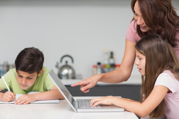 Madre con niños usando la computadora portátil en la cocina