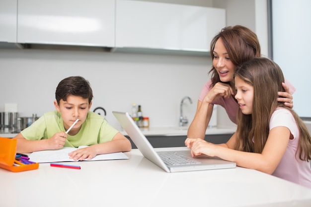 Madre con niños usando la computadora portátil en la cocina