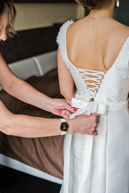 Madre de la novia ayuda a la novia a vestir un vestido.