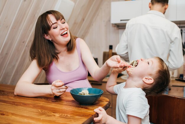 Madre con padre alimentando al niño en la cocina con pasta