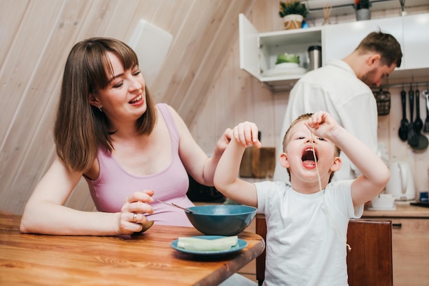 Madre con padre alimentando al niño en la cocina con pasta