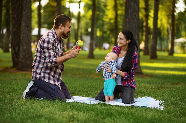 Madre, padre y bebé juegan en el césped en el parque de verano