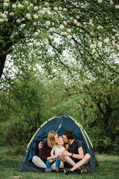 Madre, padre besa y abraza a un niño que disfruta de unas vacaciones de campamento en el campo