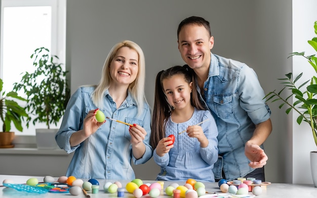 Madre, padre e hija están pintando huevos. La familia feliz se está preparando para la Pascua.