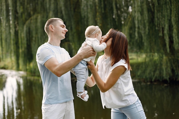 Foto madre, padre e hija pequeña de pie en el parque y posando para una foto. familia vistiendo ropa blanca y azul claro