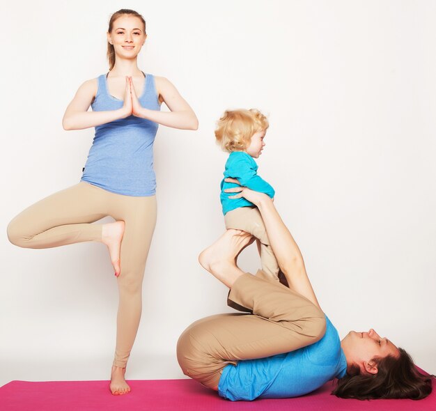 Madre, padre e hijo haciendo yoga sobre fondo blanco.