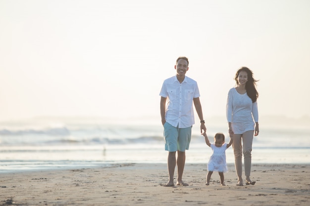 Madre y padre le enseñan a su hija a caminar por la playa