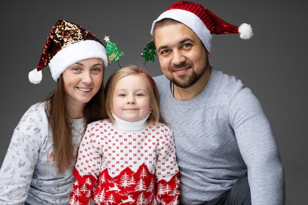 Madre y padre con gorros de santa con su hija en el medio con un aro de cabeza con dos árboles de Navidad.