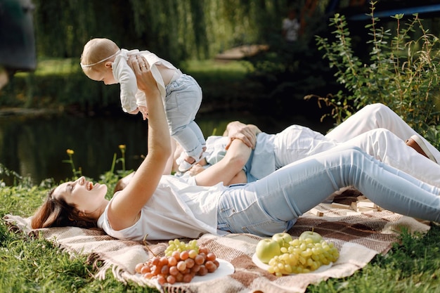 Madre, padre, hijo mayor y pequeña hija acostada sobre una alfombra de picnic en el parque. Familia vistiendo ropa blanca y azul claro