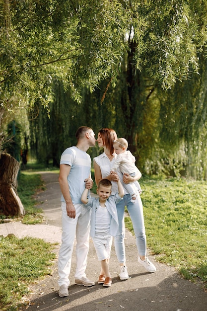 Madre, padre, hijo mayor y pequeña hija caminando en el parque. Familia vistiendo ropa blanca y azul claro