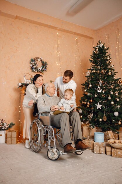 Madre padre hijo pequeño y abuelo en silla de ruedas sentado cerca del árbol de Navidad