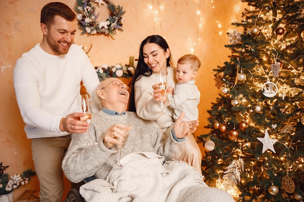 Madre padre hijo pequeño y abuelo en silla de ruedas sentado cerca del árbol de Navidad