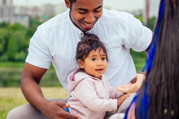 Madre y padre interraciales transnacionales caminando con su niña de raza mixta en los primeros pasos del parque de otoño