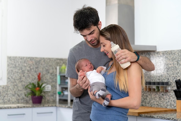 Madre y padre mirando a su bebé recién nacido y alimentándolo con biberón en la cocina