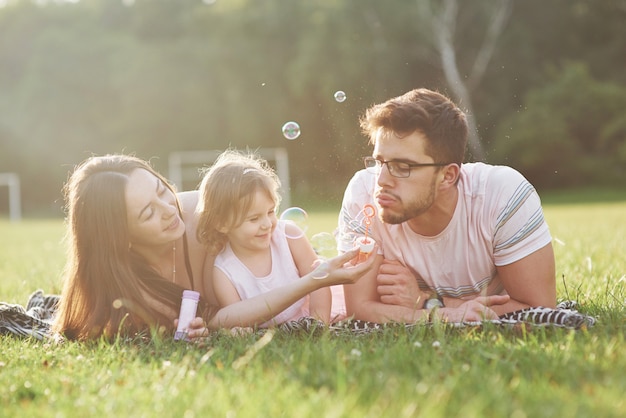 Madre y padre pasan tiempo juntos felices. Pequeña hija juega con sus padres al aire libre durante el atardecer