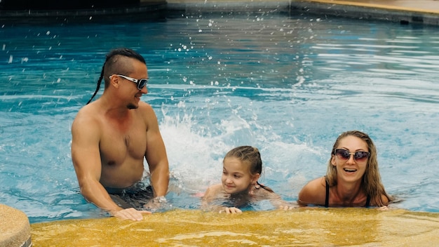 La madre y el padre con la pequeña hija se divierten en la piscina Mamá y papá juegan con el niño La familia disfruta de las vacaciones de verano en una piscina