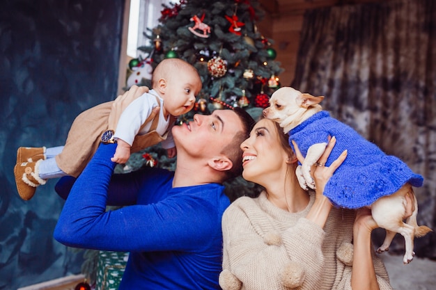 La madre, el padre, el perro y el bebé sentados cerca del árbol de Navidad