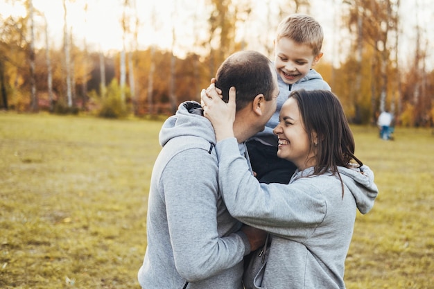 Foto madre y padre posando mientras sostienen a su hijo sobre los hombros en el parque abrazando a la familia