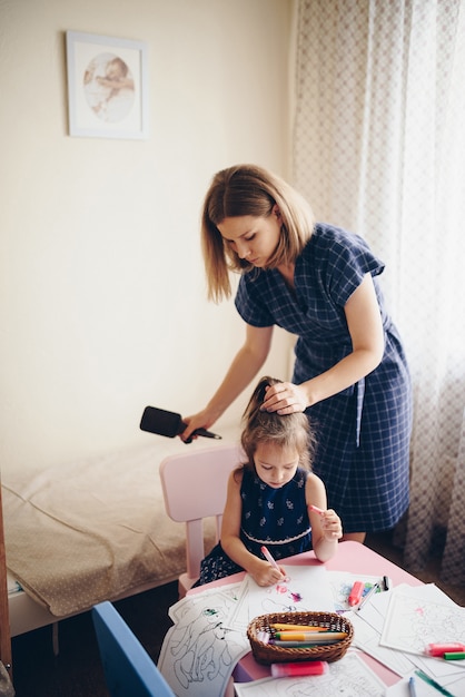 La madre peina a su hija y le hace el pelo.