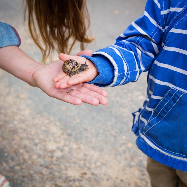 Madre y pequeño bebé hermoso del este que juegan al aire libre con un caracol