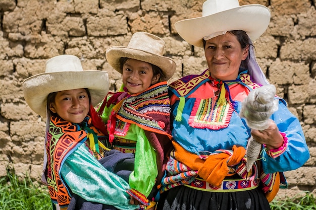 Madre peruana andina enseñando a sus hijas a tejer y hacer hilo y posar sonreír