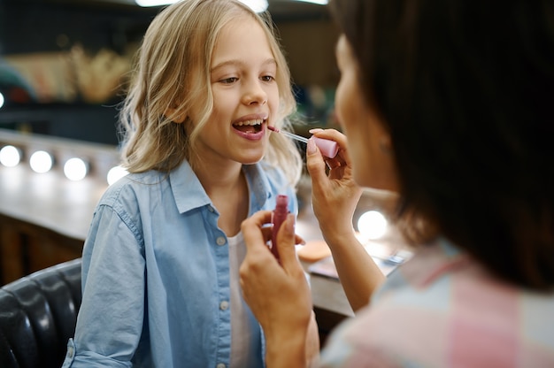 Madre pinta los labios de su hija en el salón de maquillaje