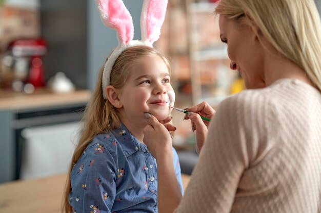 Madre pintando la cara de sus hijas con orejas de conejo