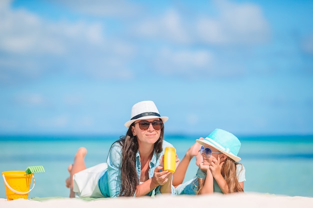 La madre pone crema de protección solar en la pequeña hija en la playa en un caluroso día de verano