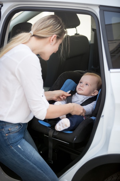 Madre que sienta a su bebé en el asiento de seguridad del automóvil